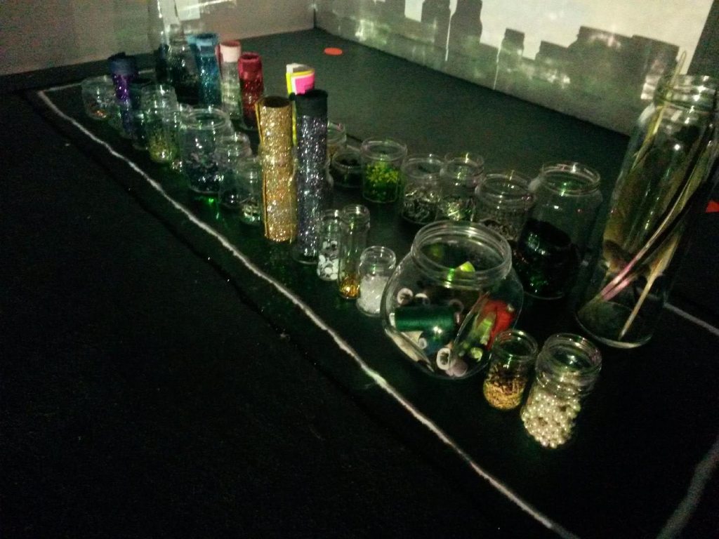 A bad quality photograph of lots of jars or crafts materials in a line with a bright light shining on them. 